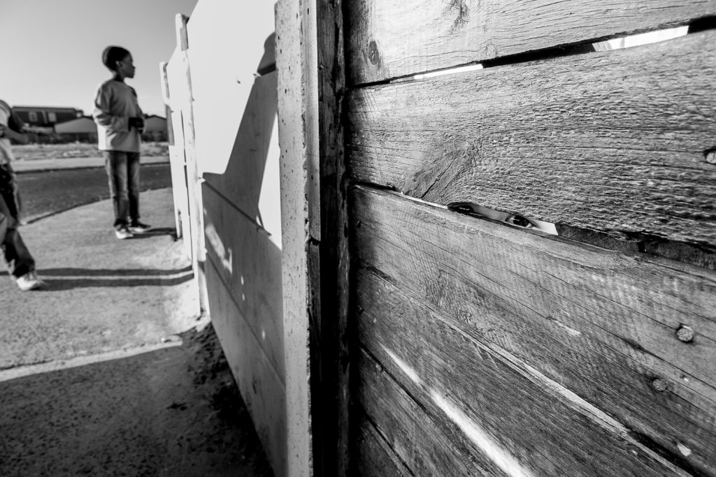 Child looking through the front gate of their home in Tafelsig, Mitchell’s Plain, 2012.